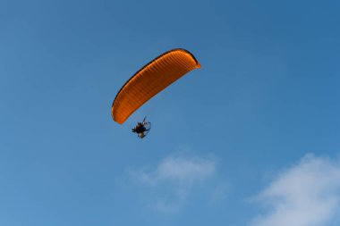 Paraglider mavi gökyüzünde turuncu bir paraglider uçuruyor. Parageleme.