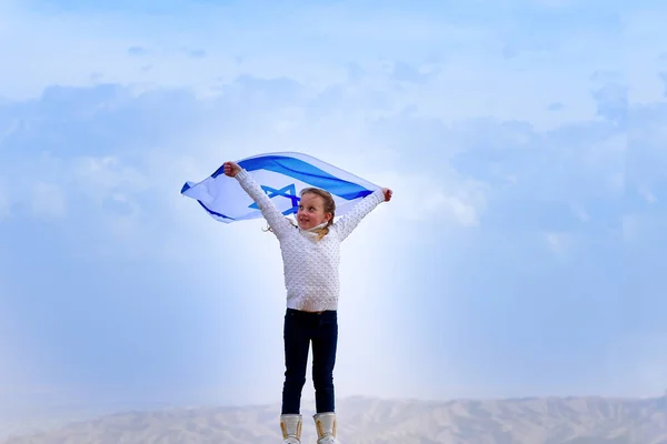 Mavi gökyüzü arka planında İsrail bayrağı olan küçük vatansever Yahudi kız.