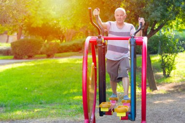Spor aletleriyle spor yapan yaşlı adam dışarıda spor salonunda çalışıyor..