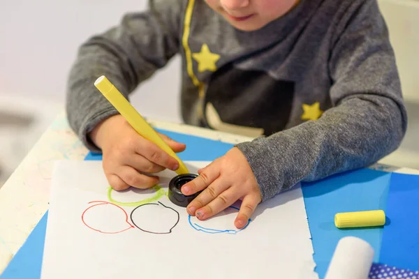Маленький малюк малює з впалими кінчиковими ручками барвисті кільця на папері . — стокове фото