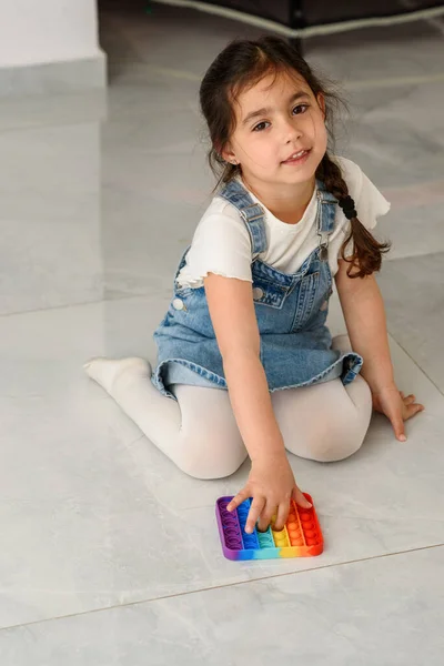 Kind sitzt auf dem Boden und spielt mit dem Fidget-Pop-Spielzeug. — Stockfoto