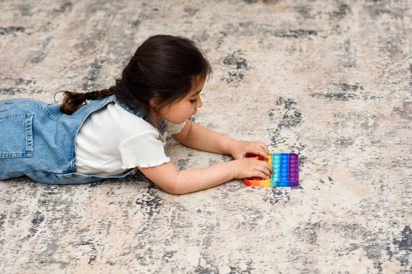 Kind liegt auf dem Boden und spielt mit dem Knall-Fidget-Spielzeug. — Stockfoto