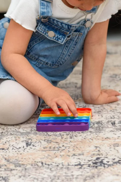 Kind sitzt auf dem Boden und spielt mit dem Fidget-Pop-Spielzeug. — Stockfoto