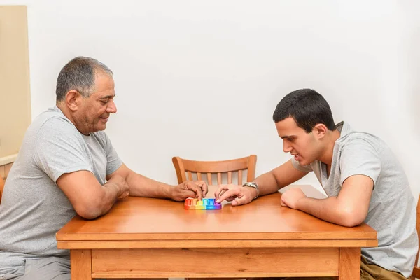 Teenager sohn und senior vater sitzen im haus und spielen mit flexiblem spielzeug der mohn fidget. — Stockfoto