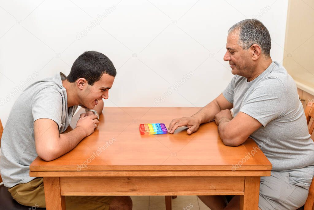 Teenager son and senior father sitting in home and playing with flexible toy the Pop It fidget.