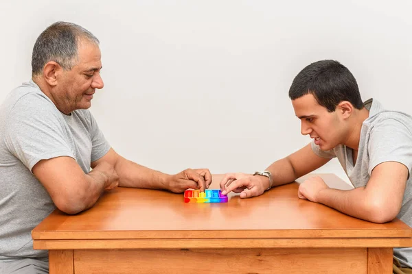 Син-підліток і старший батько сидить вдома і грає з гнучкою іграшкою поппіт . — стокове фото