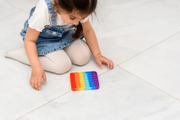 Kind sitzt auf dem Boden und spielt mit dem Fidget-Pop-Spielzeug. — Stockfoto