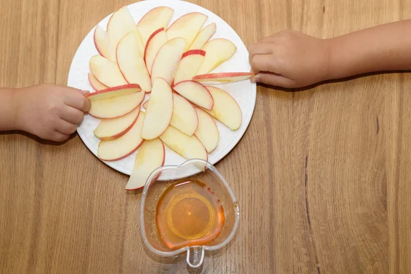 Top view apple slices on a white plate on a wooden table. Childrens hands holding slices of apple. — Stock Photo, Image