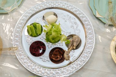 Geleneksel Hamursuz Bayramı sofrasında yumurta, kereviz, marul, charoset, acı bitki ve süslü gümüş tepside kızartılmış kemik dahil olmak üzere sembolik yiyeceklerle servis edilir..