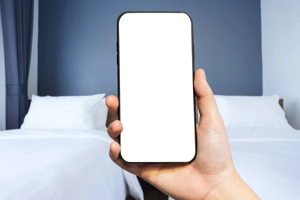 Kadın kullanımına yakın plan. Akıllı telefon, otel odasının arka planında lamba, boş zaman ve tatil konseptinde seyahat ile yatak dekorasyonu üzerine odaksız beyaz yastığın bulanık görüntülerini taşıyor.