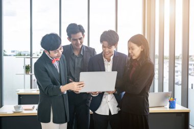 Çeşitli cinsiyetlere sahip Asyalı iş adamları grubu (LGBT), ofisteki toplantı odasındaki dizüstü bilgisayarda başarılı bir iş planı görüyor