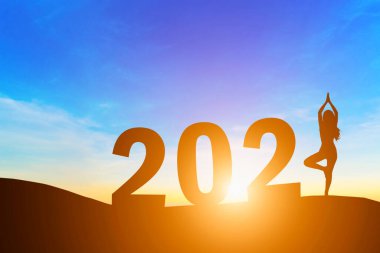 Mutlu yıllar 2021, Siluet kadını yoga yapıyor. Sabah erken saatte gün doğumunu ufukta görüyor. Sağlık ve Yeni Yıl konsepti..
