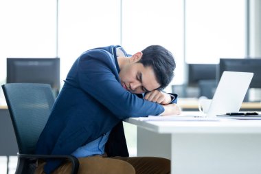 Asyalı genç işadamı geç saatlere kadar çalıştı ve ofis arka planında dizüstü bilgisayarda uyuyakaldı..