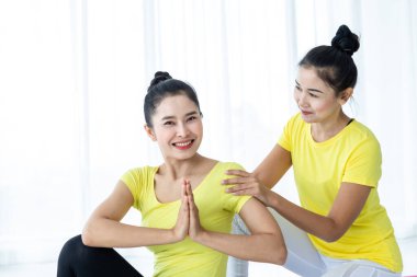 İki genç Asyalı kadın sarı elbiseyle yoga yapıyor ya da spor salonunda bir antrenörle poz veriyor ve meditasyon yapıyor sağlık yaşam tarzı ve sağlık konsepti uyguluyor..