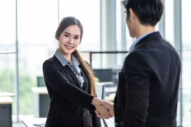 İş kadını ve işadamı, sözleşme imzalandıktan sonra ofis arka planında el sıkışırken, iş dünyası güven verici ve başarılı bir konsept olduğunu ifade etti.
