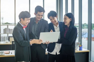 Çeşitli cinsiyetlere sahip Asyalı iş adamları grubu (LGBT), ofisteki toplantı odasındaki dizüstü bilgisayarda başarılı bir iş planı görüyor