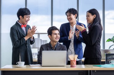 Çeşitli cinsiyetlere sahip Asyalı iş adamlarından oluşan başarılı bir grup işçi el çırpın ve iş adamını tebrik edin. Toplantı odasındaki dizüstü bilgisayarda başarılı bir iş planı görün.
