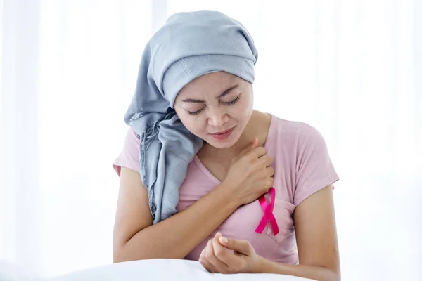 亚洲女人患乳腺癌急性心脏病患者急性心脏病症状贴粉红丝带戴头巾接受化疗后 坐在家里卧室的床上 — 图库照片