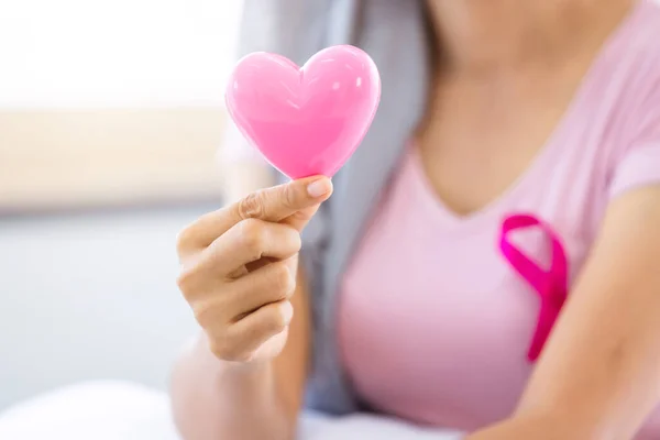 close up of women cancer patient with pink ribbon wearing headscarf After treatment to chemotherapy with holding small a pink hearts shaped at home,medicine concept