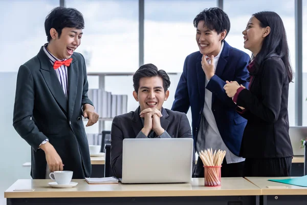 Successful happy workers Group of asian business people with diverse genders (LGBT) Clap hands and congratulate to businessman see a successful business plan on the laptop computer in the meeting room