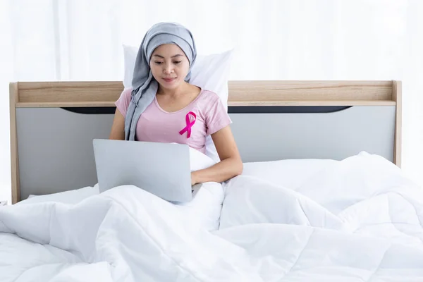 a asian women disease mammary cancer patient with pink ribbon wearing headscarf After treatment to chemotherapy with working business at laptop on bed In the bedroom at the house,healthcare,medicine