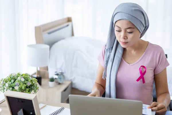 a asian women disease mammary cancer patient with pink ribbon wearing headscarf After treatment to chemotherapy with working business at laptop in office at home,medicine concept