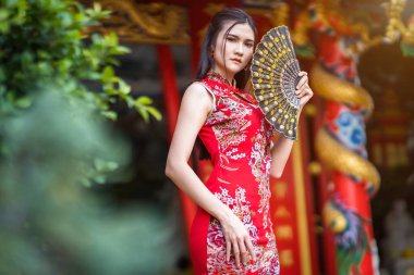 Güzel bir portre gülümseyen Asyalı genç bir kadın geleneksel Çin cheongsam süslemesi takıyor ve Tayland 'da Çin Yeni Yıl Festivali için Çin Fanning' i düzenliyor.