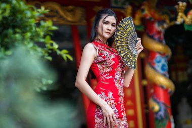 Güzel bir portre gülümseyen Asyalı genç bir kadın geleneksel Çin cheongsam süslemesi takıyor ve Tayland 'da Çin Yeni Yıl Festivali için Çin Fanning' i düzenliyor.