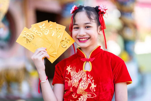 肖像画の美しい笑顔かわいいアジアの女の子は中国の神社で中国の旧正月祭りのために手に黄色の封筒を保持赤い伝統的な中国のChongsam装飾を身に着けている — ストック写真