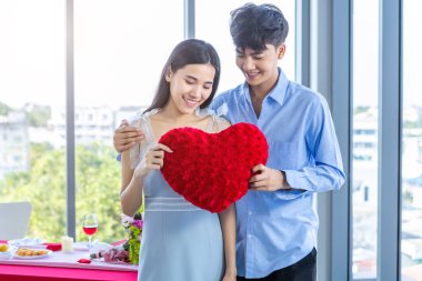 Sevgililer Günü konsepti, Asyalı genç, mutlu, aşık bir çift öğle yemeğinden sonra kırmızı kalp şeklinde yastık tutuyorlar.