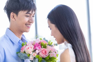 Sevgililer Günü konsepti, Asyalı genç mutlu çift, öğle yemeğinden sonra ellerinde kırmızı ve pembe güller tutuyorlar.