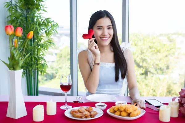 バレンタインの日のコンセプトは 笑顔幸せなアジアの若い女性がテーブルフードショーに座って レストランの背景にある小さな赤いハートを持っている — ストック写真