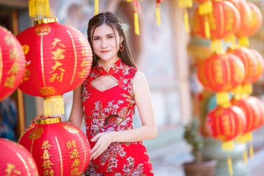 Güzel gülümseyen Asyalı genç bir kadın. Üzerinde Çin yazıları bulunan kırmızı fenerler takıyor. Kutsanmış Çin Yeni Yılı için bir övgü madalyası.