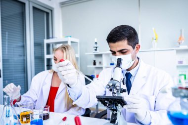 İki bilimadamı test tüpünü incelemek için kimya laboratuvarında çalışan bir bilim adamı ya da genç kadın ve erkek araştırmacı laboratuvar analizinde araştırma yapıyor.