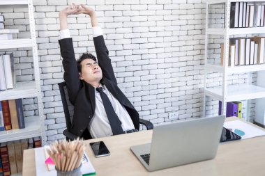 Dizüstü bilgisayardaki başarılı Asyalı genç işadamının, not defterindeki akıllı telefon ve kalemin, ofis odasındaki arka plandaki mutluluğu..