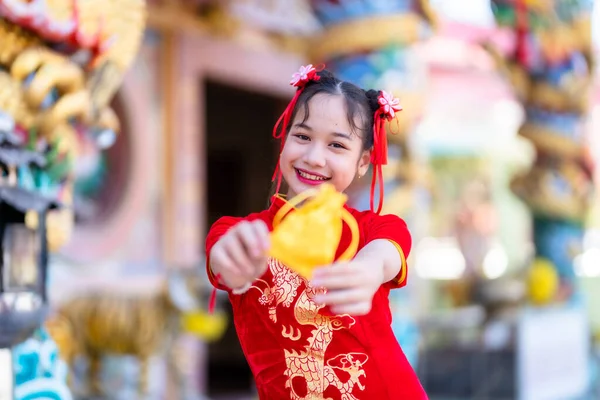 肖像画の美しい笑顔かわいいアジアの女の子を身に着けている赤い伝統的な中国のChongsam装飾フォーカスは タイの中国の神社で中国の旧正月祭りのための黄金のお金の袋を示しています — ストック写真