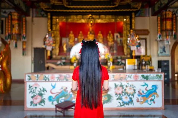 stock image beautiful Cute little Asian young woman wearing red traditional Chinese cheongsam decoration Stand for pray to buddha statue for Chinese New Year Festival at Chinese shrine in Thailand