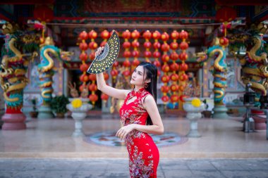 Güzel bir portre gülümseyen Asyalı genç bir kadın geleneksel Çin cheongsam süslemesi takıyor ve Tayland 'da Çin Yeni Yıl Festivali için Çin Fanning' i düzenliyor.