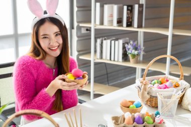 Paskalya bayramı konsepti, Mutlu Asyalı genç kadın şovu elinde renkli Paskalya yumurtaları olan bir septle beyaz oda arka planında