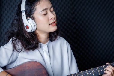 Mutlu, güzel, gülümseyen bir portre. Genç Asyalı bir vokalist. Kulaklık takıp profesyonel bir stüdyoda mikrofon önünde şarkı kaydediyor.