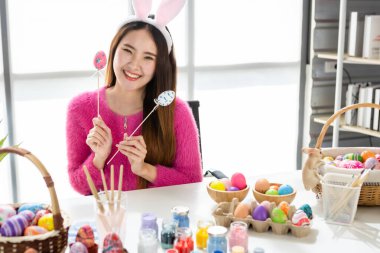 Paskalya bayramı konsepti, mutlu bir gülümseme Asyalı genç bir kadının elinde renkli Paskalya yumurtaları şiş şiş beyaz oda arka planında