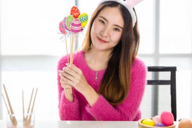 Paskalya bayramı konsepti, mutlu bir gülümseme Asyalı genç bir kadının elinde renkli Paskalya yumurtaları şiş şiş beyaz oda arka planında