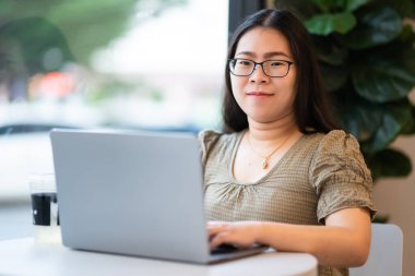 Asyalı serbest çalışanlardan memnun. İş kadını. Laptop bilgisayarı, kahve fincanı ve akıllı telefonla arka plan, iletişim konsepti gibi yerlerde çalışıyor.