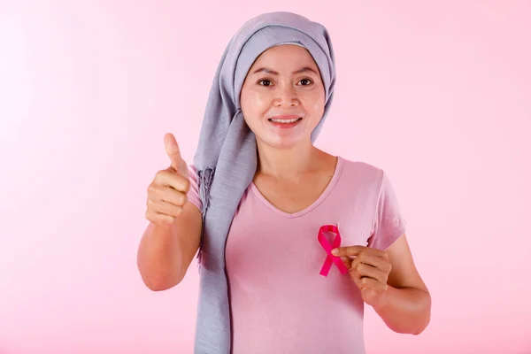 a asian women disease mammary cancer patient in pullover holding pink ribbon and showing thumbs up isolated on pink blank copy space studio background,healthcare,medicine concept