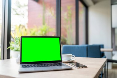 Kahve dükkanının arka planında boş ekranlı ve akıllı telefonlu dizüstü bilgisayarın bir kopyası, yeşil ekran.