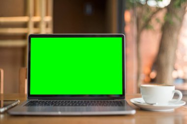 Kahve dükkanının arka planında boş ekranlı ve akıllı telefonlu dizüstü bilgisayarın bir kopyası, yeşil ekran.
