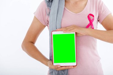 Asyalı bir kadın pembe meme kanseri farkındalığı kurdelesi olan boş bir tablet kullanıyor. Beyaz fotokopi stüdyosu arka planı, sağlık sigortası, tıp konsepti, yeşil ekran.