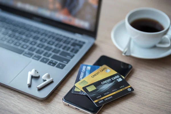 Close-up of Credit card of Keyboard laptop computer, wireless earphones and smartphone empty screen on wooden background office desk in coffee shop like the background