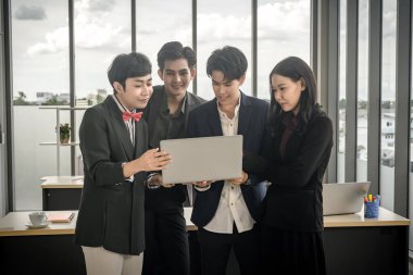 Çeşitli cinsiyetlere sahip Asyalı iş adamları grubu (LGBT), ofisteki toplantı odasındaki dizüstü bilgisayarda başarılı bir iş planı görüyor