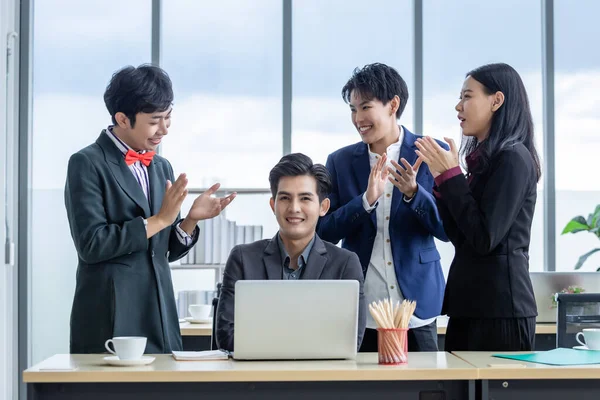 Successful happy workers Group of asian business people with diverse genders (LGBT) Clap hands and congratulate to businessman see a successful business plan on the laptop computer in the meeting room